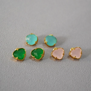 Macro shot of three pairs of heart-shaped gemstone earrings in blue, green and pink colors