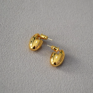 Macro detail of high-polished gold egg-shaped stud earrings on grey fabric background