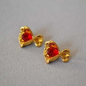 Macro detail of candy-shaped gold earrings featuring large faceted red zircon stones