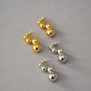 Close-up of stacked gold and silver metallic ball earrings with mirror finish texture
