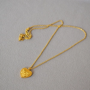 Detail of vintage gold heart pendant with quilted pattern on a textured gray surface