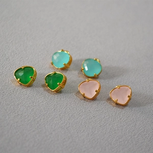 Close-up of three pairs of heart-cut gemstone studs in green, blue, and pink with gold plating