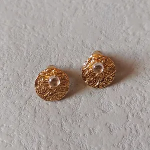 Macro shot of 925 silver needle stud earring with textured gold finish and white gemstone