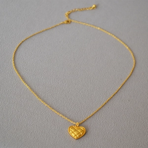 Detailed macro view of gold quilted heart pendant with fine beaded edges and cross chain
