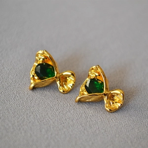 Detail view of gold candy-shaped stud earrings with emerald green zircon stones