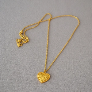 Close-up of golden heart pendant with quilted texture and bead edge on cable chain