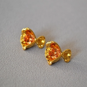 Detailed shot of gold-toned earring with orange zircon and crumpled petal texture
