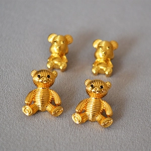 Macro detail of four cute golden striped bear stud earrings on grey fabric background