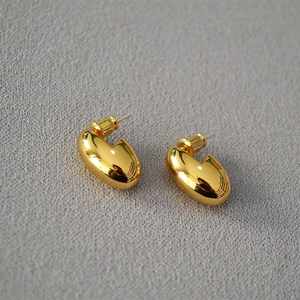 Minimalist golden bean stud earrings with a high-polished finish on a textured background