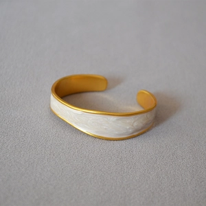 Detail view of vintage gold brass bangle with white enamel inlay and open C-shape design
