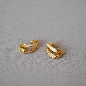 Close-up of gold ear studs with white enamel inlay and sparkling zircon crystals