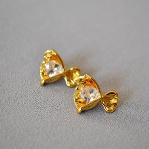 Detailed view of gold crinkle candy flower studs with clear faceted zircon on fabric