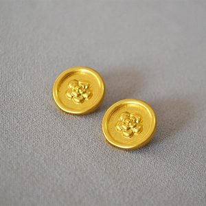 Detail view of vintage matte gold camellia embossed stud earrings on grey fabric