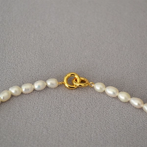 Elegant freshwater rice pearl necklace with golden double ring clasp on dark background