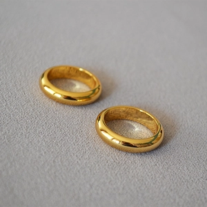 Detail view of two polished gold-plated brass rings on a soft gray textured background