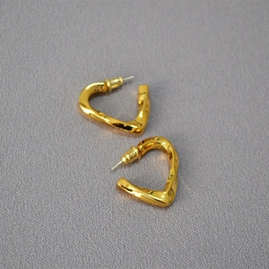 Macro shot of twisted heart earrings in polished gold finish on grey textured fabric