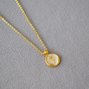 Macro detail of golden rose flower pendant with white enamel on a sleek chain