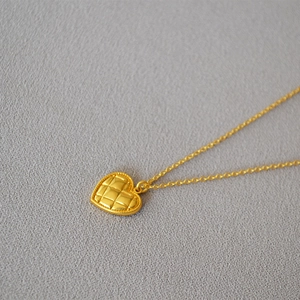 Close-up of matte gold heart pendant featuring a classic quilted pattern and beaded edge