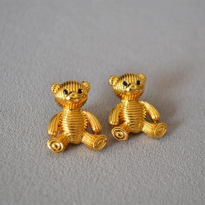 Close-up of golden striped bear stud earrings with 925 silver needles on grey fabric