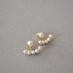 Detailed view of elegant gold curved stud earrings with gradient pearls on textured fabric