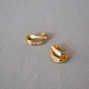Close-up of golden C-shaped double-layered earrings with white enamel and square zircons