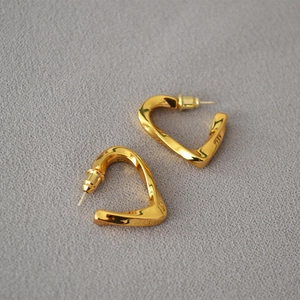 Detailed macro view of twisted gold-plated heart earrings on textured grey fabric
