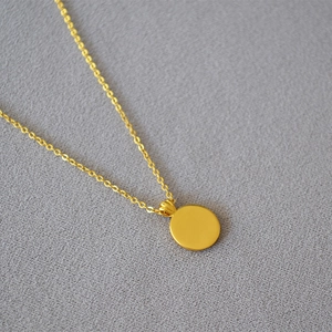 Detail shot of the polished gold coin pendant with a delicate cross chain on grey texture