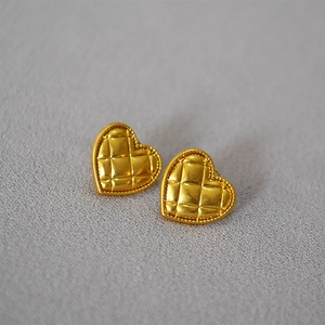 Detail of heart-shaped gold plated earrings with quilted texture and beaded edge