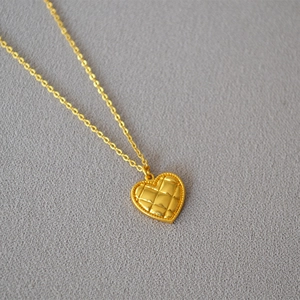 Detail of vintage heart pendant featuring quilted pattern and golden bead edge