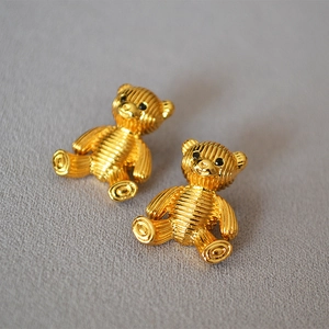 Macro shot of cute golden striped bear stud earrings on grey textured fabric
