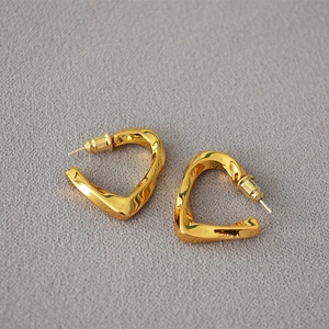 Detail of twisted gold earrings with a polished metallic finish and geometric heart design