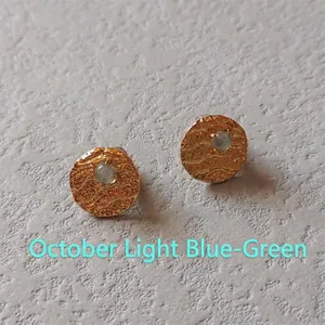 Detail of gold textured stud earrings with light blue-green gemstone for October