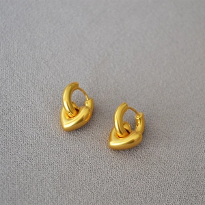 Dettaglio degli orecchini a cuore placcati in oro su sfondo in tessuto grigio testurizzato