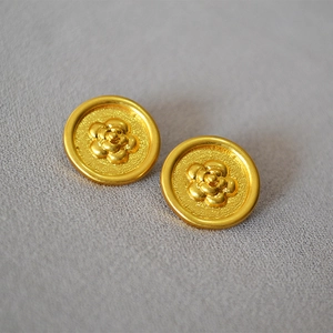 Macro shot of vintage gold camellia flower stud earrings with a matte textured finish
