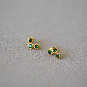 Close-up of three-stone cluster earrings with green zircons in a gold-plated setting