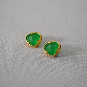 Detail of green emerald-cut gemstones in gold-plated claw settings on a gray texture