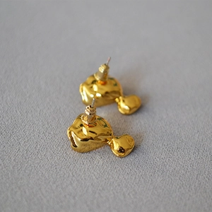 Detail view of irregular molten gold earrings with a polished liquid texture on grey fabric