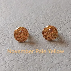 Macro shot of 11th birthstone earrings with hammered metal texture and pale yellow stone