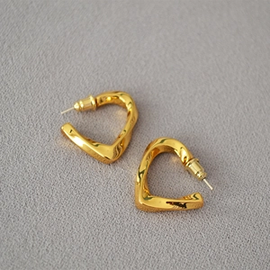 Detailed close-up of golden twisted heart-shaped earrings on textured gray cloth