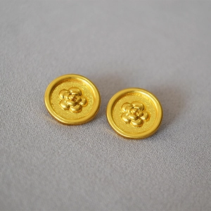Macro detail of gold-plated camellia flower relief studs with matte textured finish
