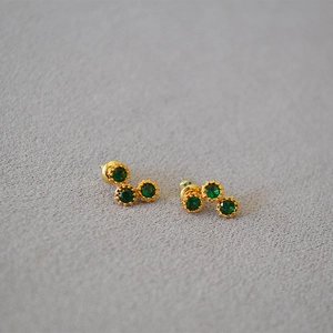 Detailed macro view of gold earrings featuring three green zircon stones in a vintage setting