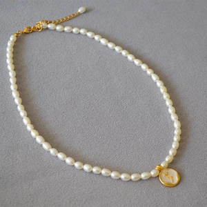 Close-up of pearl necklace with a vintage gold rose relief pendant on white enamel