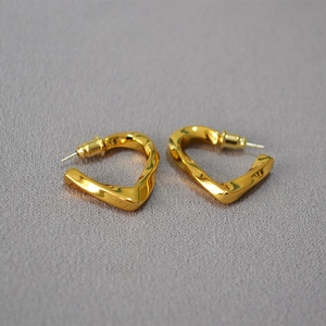 Macro detail of gold-plated twisted heart stud earrings on grey fabric texture