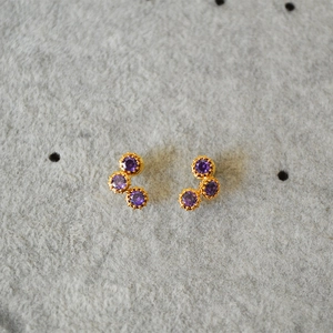 Macro detail of gold earrings featuring three purple round-cut cubic zirconia stones