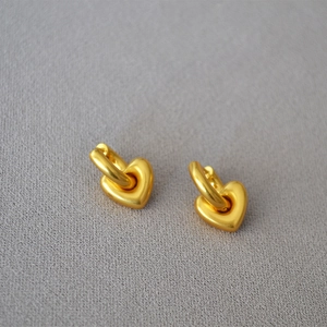 Orecchini a cuore in oro opaco su sfondo in tessuto grigio in stile minimalista