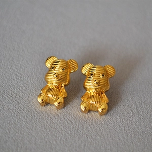 Macro detail of golden bear stud earrings with horizontal striped texture and glossy finish