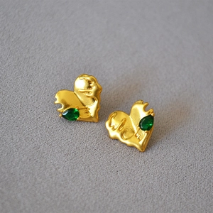 Macro shot of molten gold heart earrings with tear-shaped green emerald stones