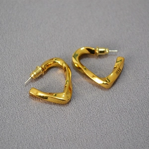 Detail of twisted heart-shaped gold earrings with polished finish on dark fabric