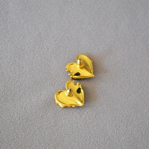 Detailed macro view of heart-shaped gold earrings with emerald green gemstones
