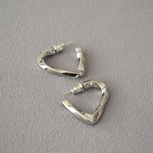 Close-up of twisted heart-shaped silver earrings on textured fabric background
